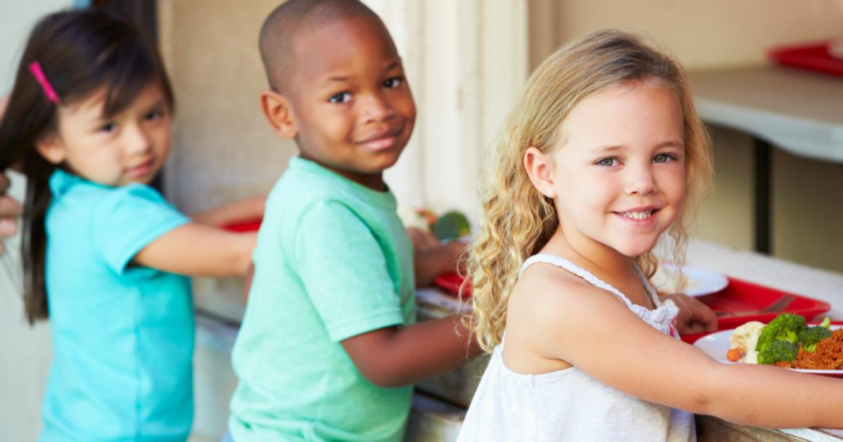 Children smiling for camera during school lunch